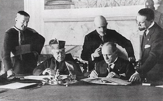 1929, Benito Mussolini i Kardynał Pietro Gaspari. Podpisanie Traktatów laterańskich, regulujących relacje między państwem a kościołem. Traktaty uznawały papieża za osobę świętą a religię katolicką za panującą w kraju, źródlo: sites.google.com https://www.sites.google.com/site/paulroebling/home/how-christian-religious-fanatics-kill-gay-teenagers-part-three